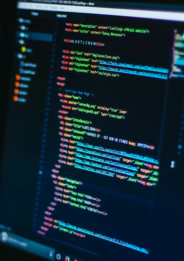 Ein Computerbildschirm zeigt HTML-Code, der in einem Texteditor geschrieben wurde. Er präsentiert ein Webdesign mit Tags für Metadaten, Stil und Navigationsmenü. Die Editoroberfläche verfügt über Zeilennummern und farbcodierte Syntax, während die Raumbeleuchtung Reflexionen auf dem Bildschirm erzeugt.