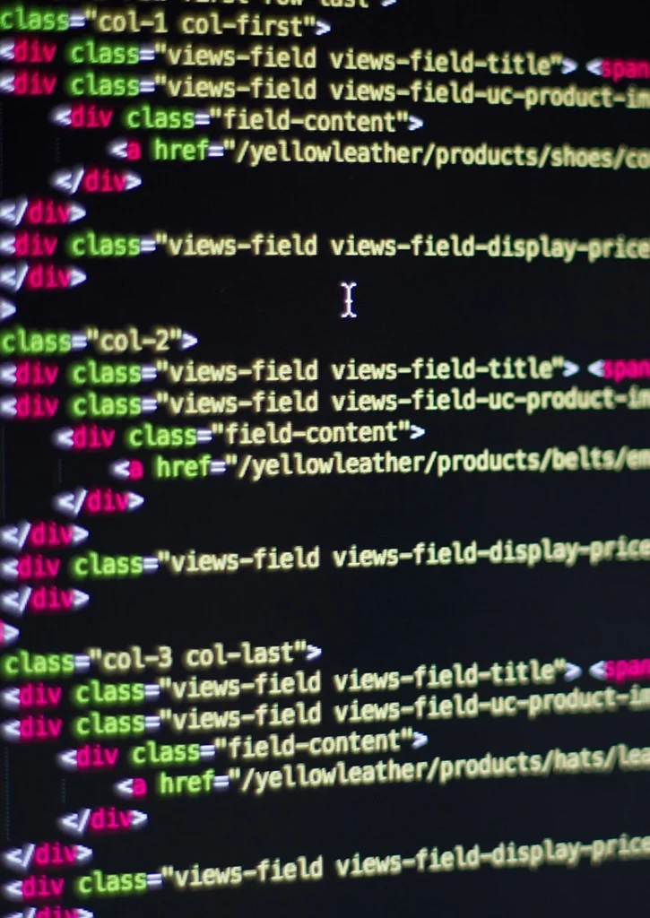 Nahaufnahme eines Computerbildschirms mit HTML-Codezeilen, der komplexes Webdesign veranschaulicht. Der Code enthält verschachtelte Div-Elemente mit Klassen wie „col-1 col-first“ und „views-field“. Links sind grün hervorgehoben, während andere Elemente in leuchtenden Farben auf schwarzem Hintergrund erscheinen.